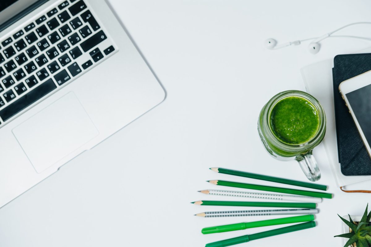 Healthy desktop with green smoothie and laptop on white background. Top View Space for Text